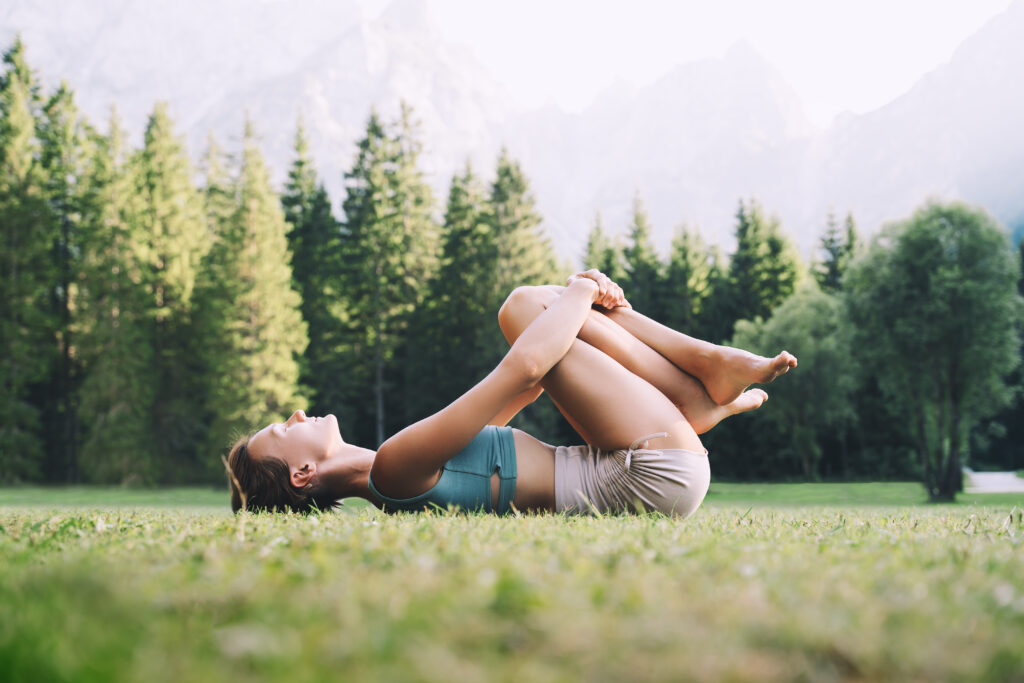 Young woman practicing the knee to chest yoga stretch in nature.